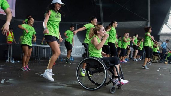 Diferents persones en un escenari dirigint les activitats de fitnes, entre ells, una noia amb cadira de rodes