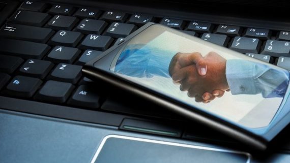 Handshake reflected on a smartphone placed on a laptop.