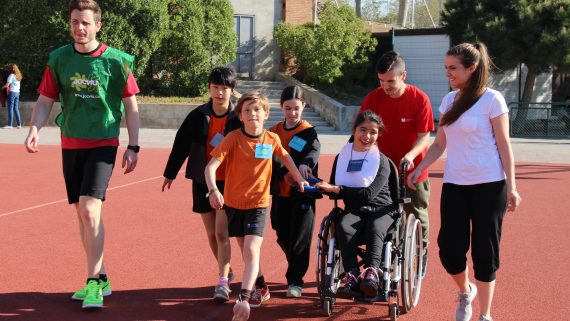 Grupo de niños y niñas corriendo en una pista de atletismo con una niña en silla de ruedas