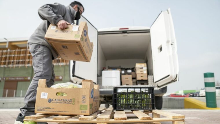 Un transportista d’una botiga de queviures ecològics carrega caixes de verdures a la seva camioneta a l’exterior del Biomarket