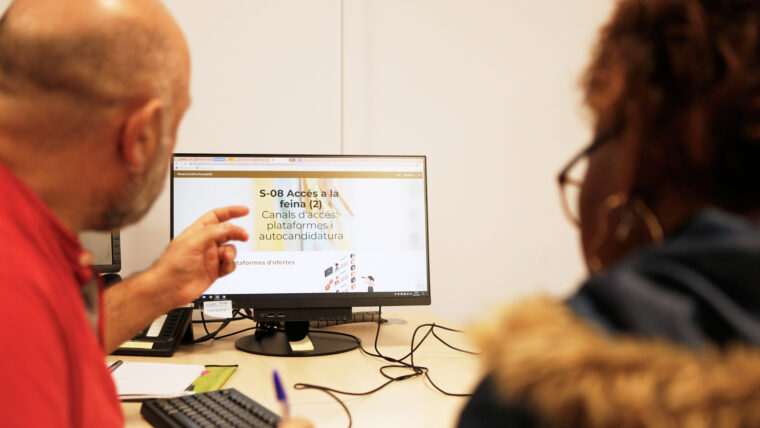 Una taula d'escriptori amb un home assenyalant una pantalla d'ordinador on posa: Accés a la feina mentre parla amb una dona.