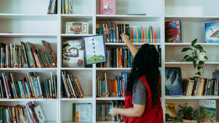Una treballadora col·loca llibres a la Biblioteca de l'Escola Mercè Rodoreda a la Prosperitat