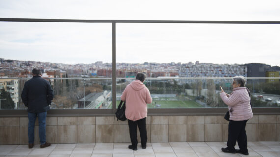 Three people take in the views from a terrace, where a football ground can be seen