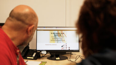 Dues persones mirant una pantalla on posa: Accés a la feina.