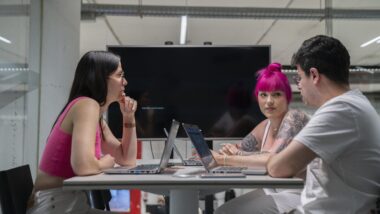 Tres noies amb tres ordinadors treballen en una sala comuna.