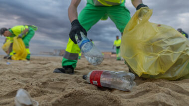 Un treballador de la neteja recull ampolles de plàstic a la platja