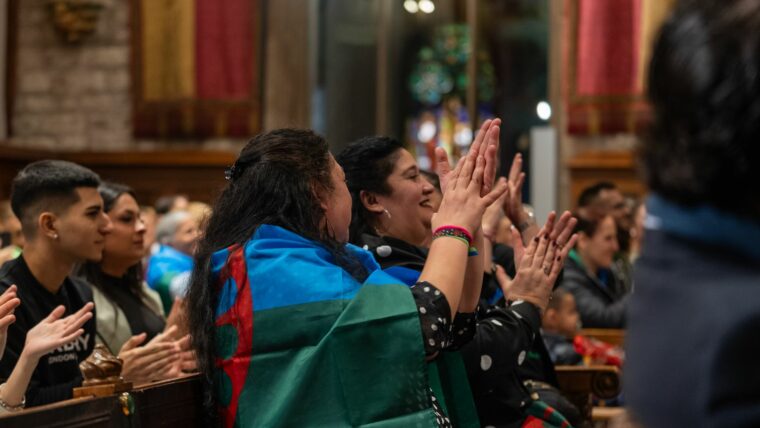 Dues persones amb banderes del poble gitano a l'esquena aplaudeixen.
