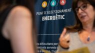 Una treballadora del Punt d'Assessorament Energètic, dona informació a una usària. Es veu un cartell del centre amb informació genèrica el servei.