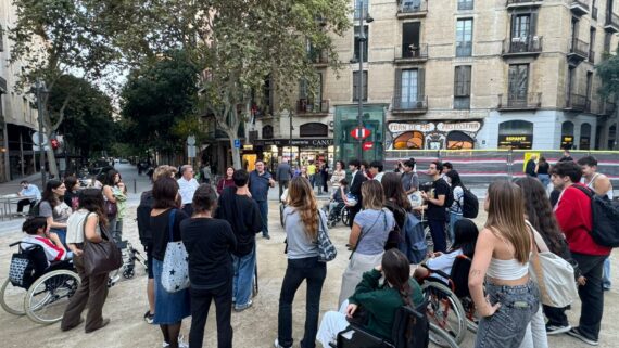 Joves adolescents en mitjana rotllana al carrer escoltant les explicacions. Algunes persones van amb cadira de rodes.