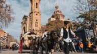 Dos nois, caracteritzats, desfilant pel carrer de Torras i Bages amb un dels carros de cavalls de la festa dels Tres Tombs del barri de Sant Andreu. De fons, la parròquia de Sant Andreu de Palomar.